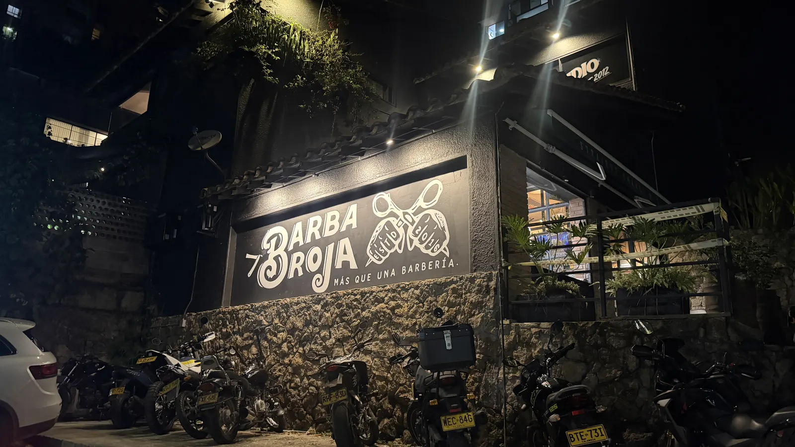 Fachada nocturna de Barba Roja Co. con el mural pintado a mano: Más que una barbería